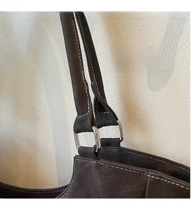 Close-up of contrast stitching and silver hardware on dark brown leather tote bag