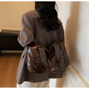 Detail of the large brown tote bag showing the glossy texture and metal buckle accents