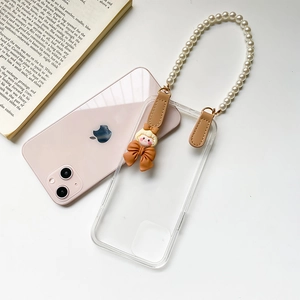 Détail coque iPhone transparente avec bracelet perles et breloque poupée sur un livre
