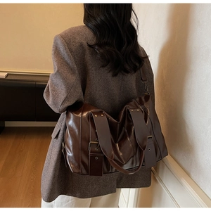 Detail of dark brown tote bag showing wide leather strap and bronze metal buckles