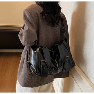 Detail of black glossy tote bag featuring vintage metal buckles and adjustable straps