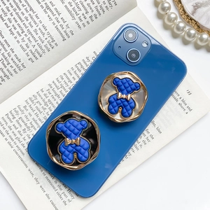 Detail of blue teddy bear phone grip with gold bow on a blue smartphone case