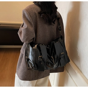 Detail of a black vintage tote bag with metallic buckle and rivet accents on a model