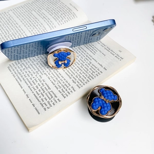 Detail showing the royal blue bear pop socket with gold bow on a mobile phone