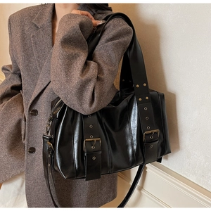 Detail of vintage black glossy leather tote bag with rivets and metal buckles on a model