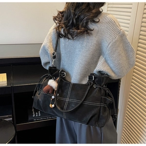 Detail der schwarzen Shopper-Tasche mit Kontrastnähten und Plüsch-Anhänger