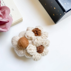 Detailed knit flower phone stand with brown center and cream petals on a vintage background