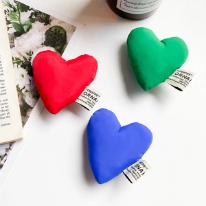 Three colorful plush heart charms with Creative labels on a minimalist white desk
