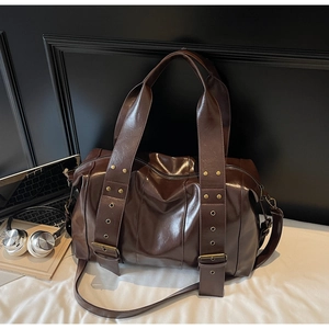 Detail of dark brown oil-wax leather tote with metal rivets and bronze buckles