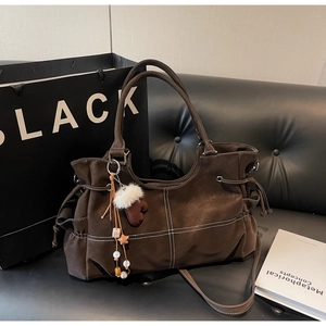 Detail of dark brown matte tote bag with white stitching and plush glove charm accessory