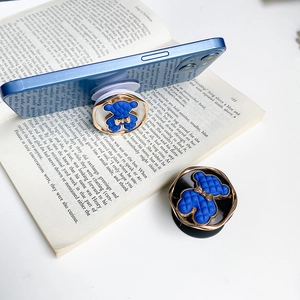 Blue teddy bear phone grip with metallic finish and gold bow on a stylish smartphone