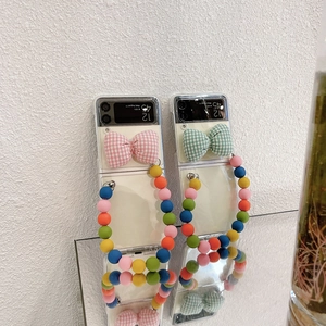 Detail of clear Z Flip phone case featuring plaid bow decorations and colorful beaded strap