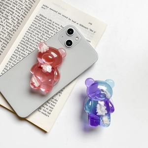 Close-up of 3D bear phone grips in red and blue gradient on a minimalist white desk