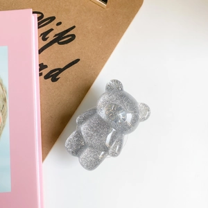 Supporto per telefono a forma di orsetto glitterato argento su sfondo scrivania bianco