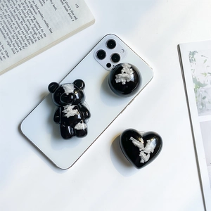 Close-up of black bear and heart shaped phone grips with white marble texture on a phone