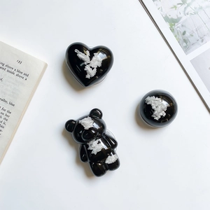 Close-up of black glossy heart, bear, and dome collapsible phone sockets on white background