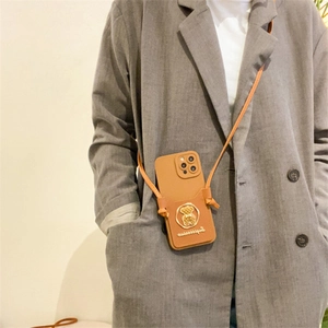 Brown leather phone case featuring a gold bear emblem and crossbody strap on a grey suit