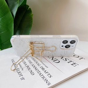 Close-up of clear iPhone case with gold foil and metal binder clip kickstand on a book