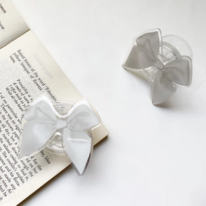 Close-up of a grey fabric bow phone grip on a transparent acrylic base over a book