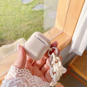 Κοντινό πλάνο κρεμ θήκης AirPods με χοντρή αλυσίδα ρητίνης σε φυσικό ηλιακό φως