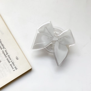 Detail of grey fabric bow phone grip with clear acrylic case on a white desk