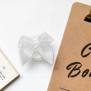 Macro detail of white satin bow phone grip with clear acrylic base on aesthetic background
