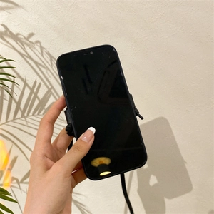 Black iPhone case with crossbody lanyard strap shown being held against a beige wall
