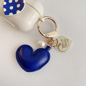 Detail of blue leather heart keychain with pearl and engraved gold heart on earphone case