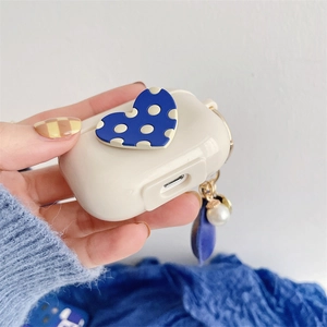 Creamy Airpods case with blue polka dot heart and pearl charm held in hand