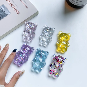 Detailed view of six colorful glitter bear phone grips on a minimalist white desk