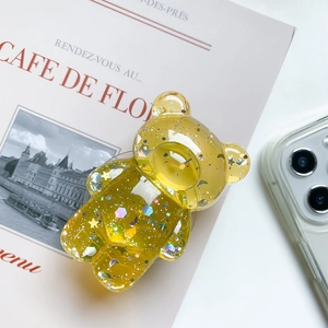 Detail of transparent bear phone grip with colorful sequins on a magazine background