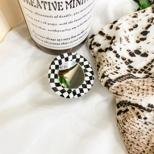 Detail of a checkerboard phone grip mirror placed on a minimalist fabric background