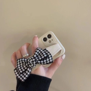 Close-up of white iPhone case featuring a black and white houndstooth bow wristband strap