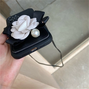Detail view of black phone case featuring white camellia flower and pearl lanyard strap