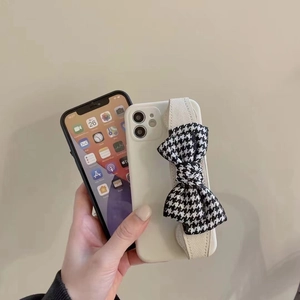Close-up of matte white iPhone case featuring a houndstooth bow wrist strap handle