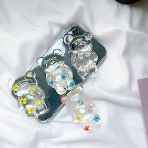 Close-up of transparent bear phone grips with colorful dried flower inserts on white fabric