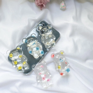 Detailed view of resin bear phone grips with colorful dried flower inserts on white fabric