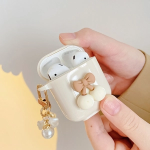 Detail of cream AirPods case with brown bow, cherry accent and pearl floral pendant charm