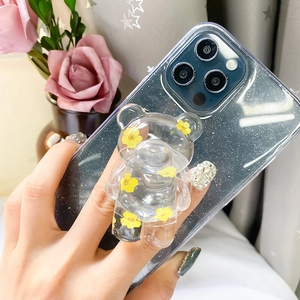 Detail of transparent bear phone grip with yellow dried flowers on a clear glitter case