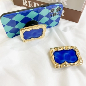 Detail of blue checkerboard phone case and gold baroque pop sockets on white fabric