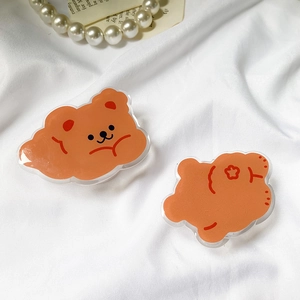 Detail view of two cute orange acrylic bear phone grips on white fabric with pearls