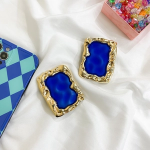 Detail of Klein blue resin inlay in gold lava-textured rectangular earrings on white fabric
