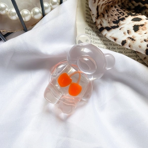 Detail of cute transparent bear phone grip with orange cherry decor on white fabric