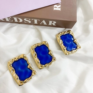 Detail of blue enamel inlay on rectangular gold wavy edge accessories set on white silk