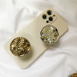 Detail showing two gold metallic textured phone grips on a beige case over white fabric