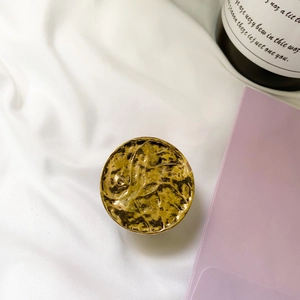 Detailed view of round golden hammered metal phone grip on white silk background