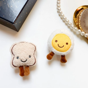 Macro detail of plush toast and poached egg phone grips with cute embroidered faces