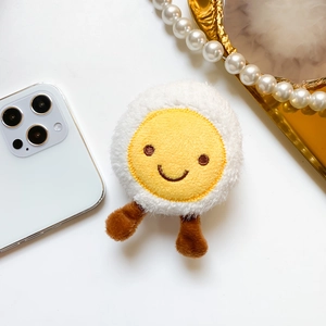 Close-up of cute plush egg phone socket grip with embroidered smiling face and soft texture