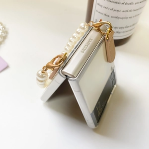 Detail of clear Samsung Z Flip case featuring elegant pearl wrist strap and pink charm