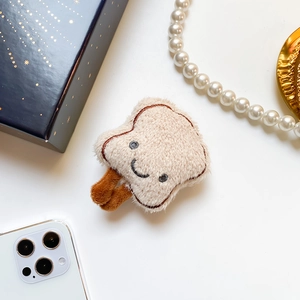 Detailed close-up of cute plush toast phone grip with embroidered smiley face and small legs